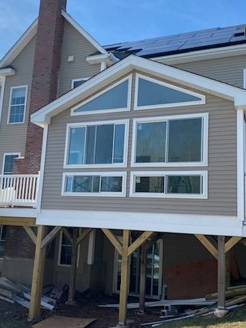 Tan house addition with large windows and a deck, under construction.