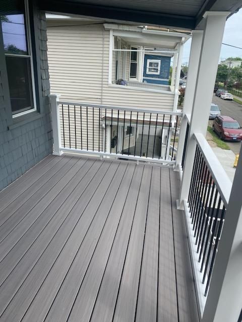 Gray wooden deck with black railings and white posts. Street and houses visible in the background.