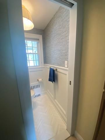 Narrow bathroom with white wainscoting, textured gray wallpaper, and herringbone floor.