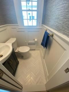 Small bathroom with white walls, herringbone tile floor, toilet, sink, and window.