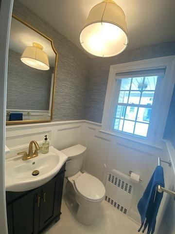 A well-lit powder room features a white toilet, black vanity with gold fixtures, a gold-framed mirror, and a window.