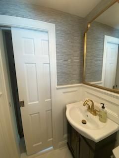 White bathroom with a sliding door, sink with gold fixtures, and textured wallpaper.