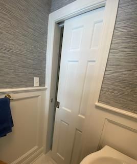 White door ajar in bathroom, slightly tilted. Gray textured wallpaper, white trim.