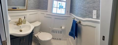 A small, white bathroom with a toilet, sink, and blue towel. The walls are decorated with a pattern.