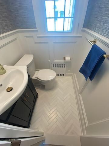 Small bathroom with white walls, herringbone tile floor, toilet, sink, and a blue towel.