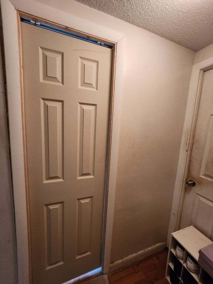 Beige door with six panels in a doorway, next to a stained wall and another open door.
