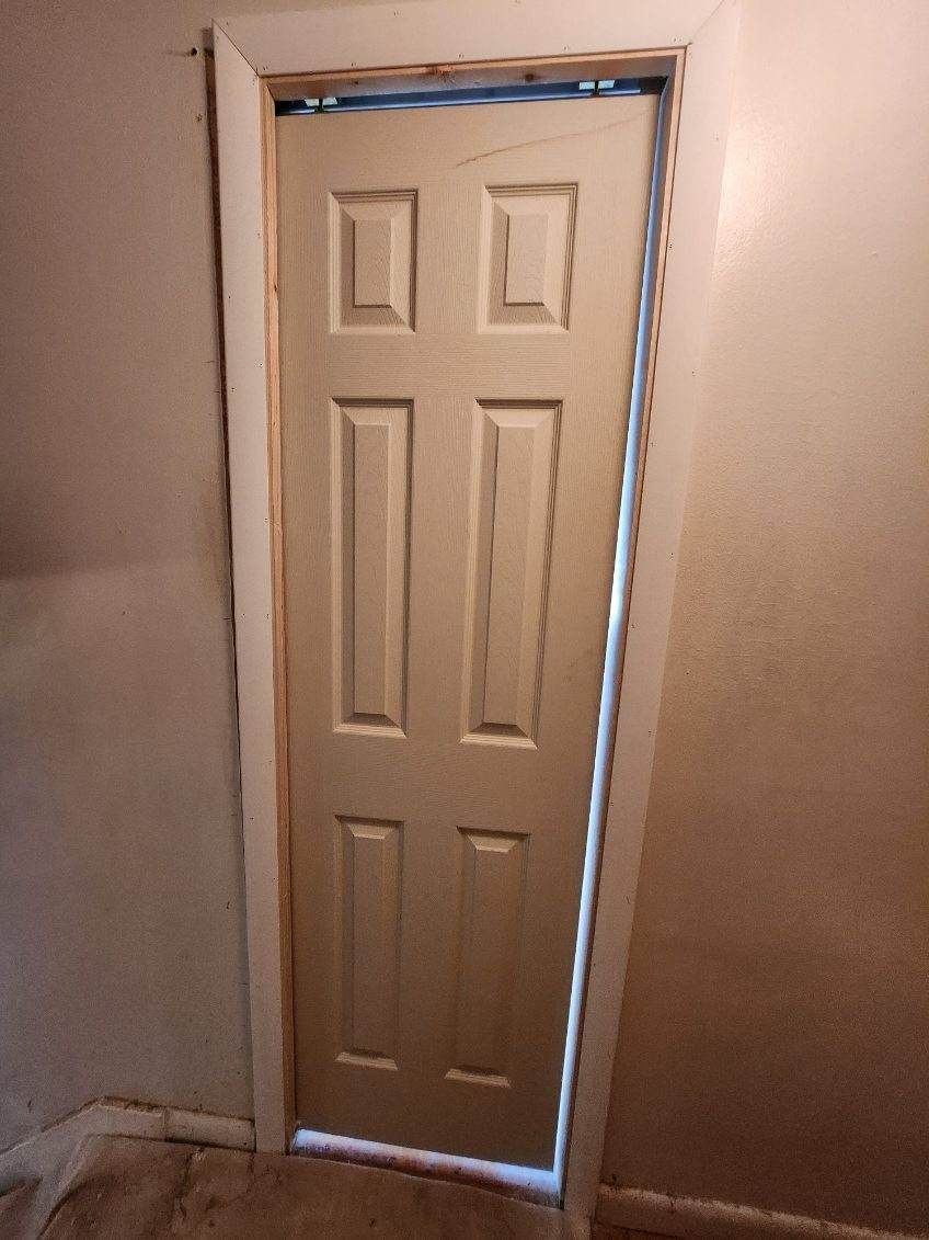 Tan door with six panels slightly ajar in a doorway, set against beige walls.