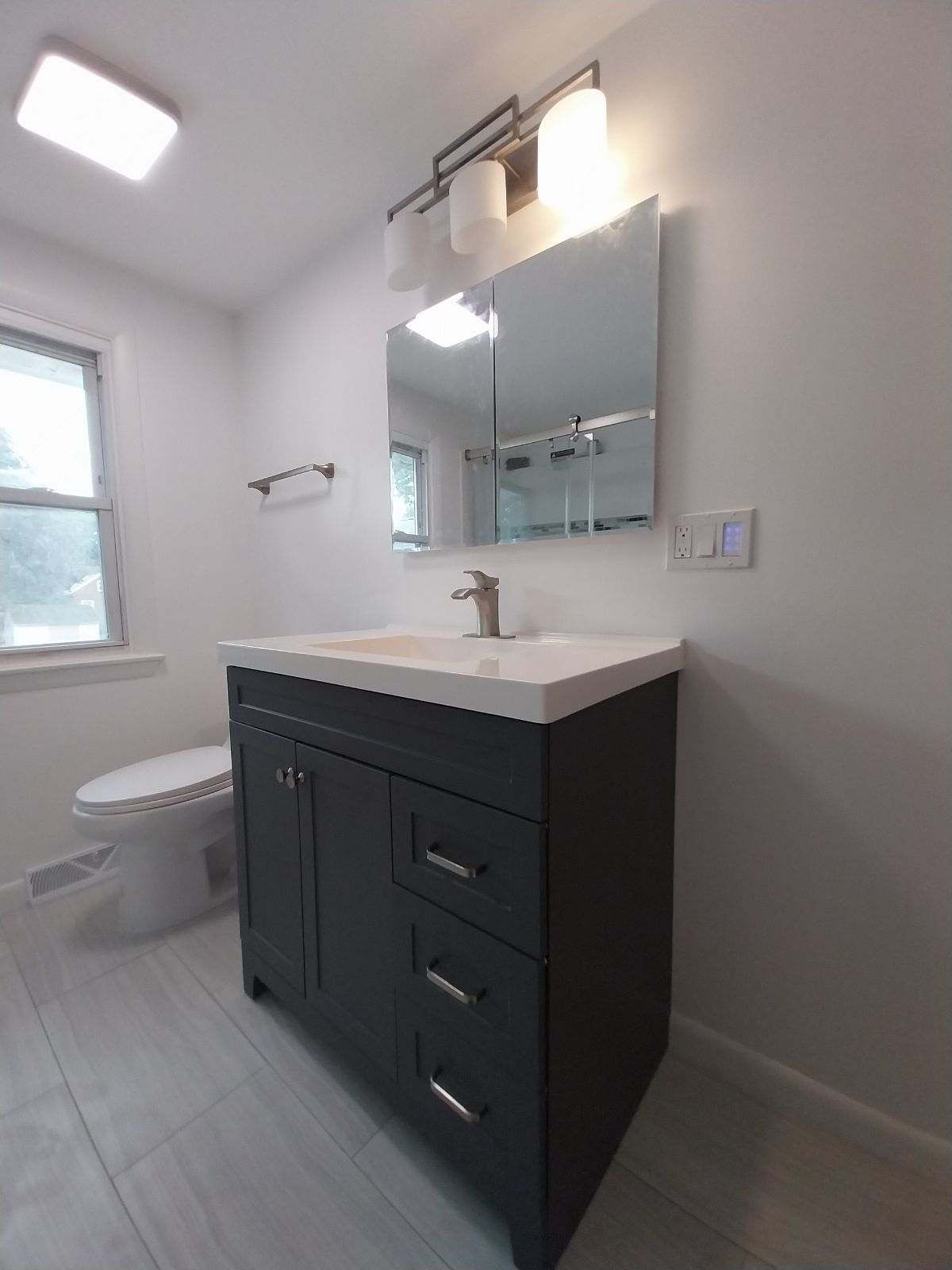 Dark gray bathroom vanity with a white countertop and mirror; white walls.