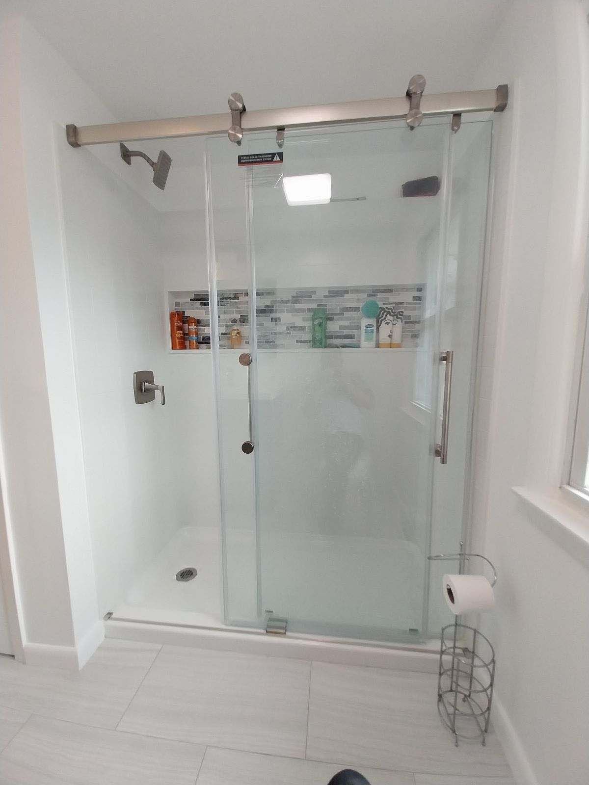 Glass shower enclosure with sliding door and stainless steel hardware in a white bathroom.