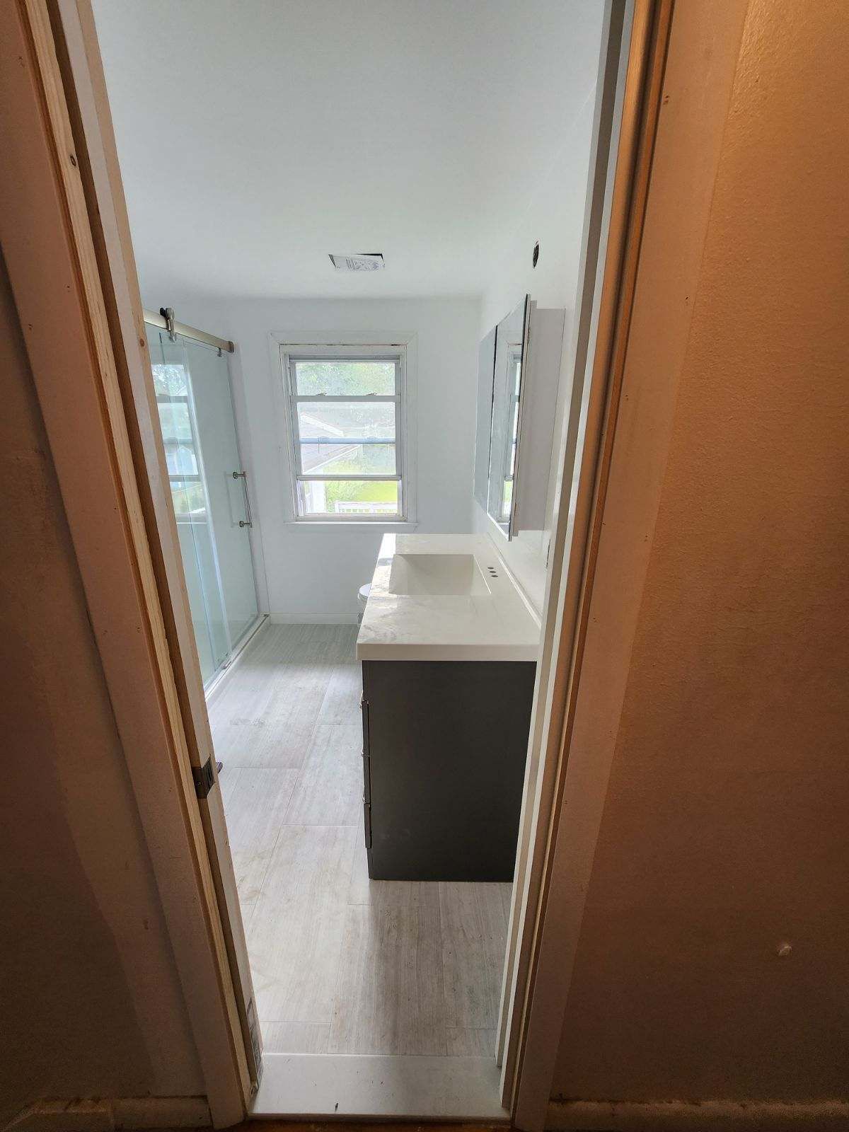 Bathroom viewed from doorway: double vanity with gray cabinet, large window, glass shower.