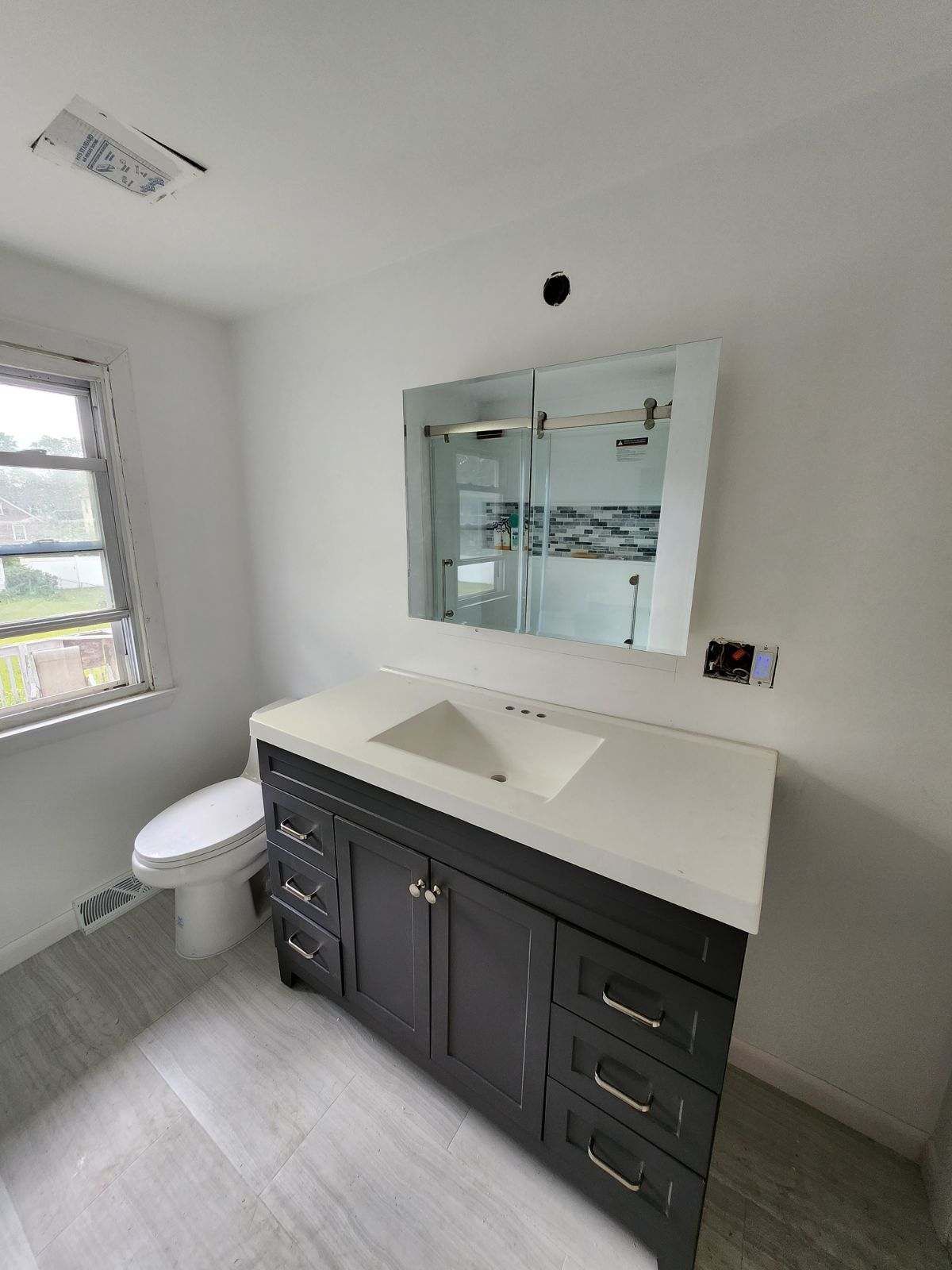 Bathroom with dark vanity, white countertop, large mirror, and toilet. Gray flooring and white walls.
