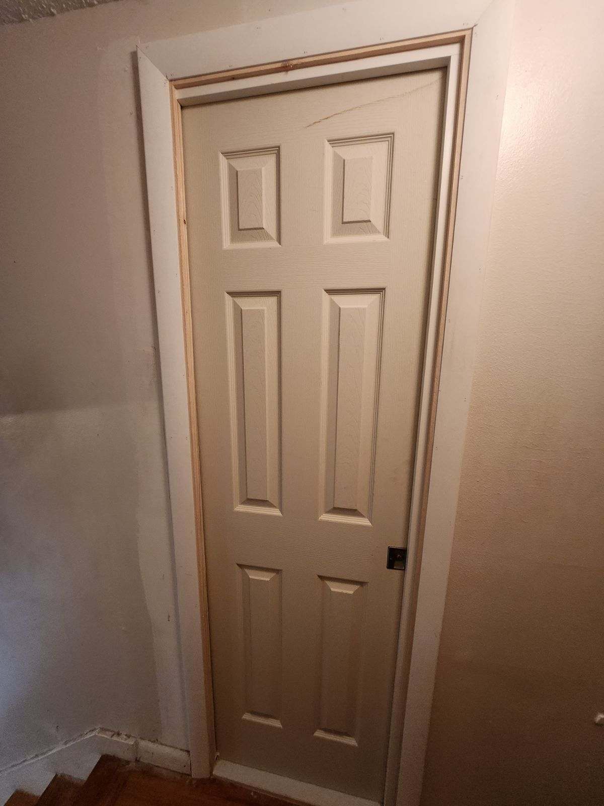White six-panel door in a hallway, surrounded by white trim and beige walls.