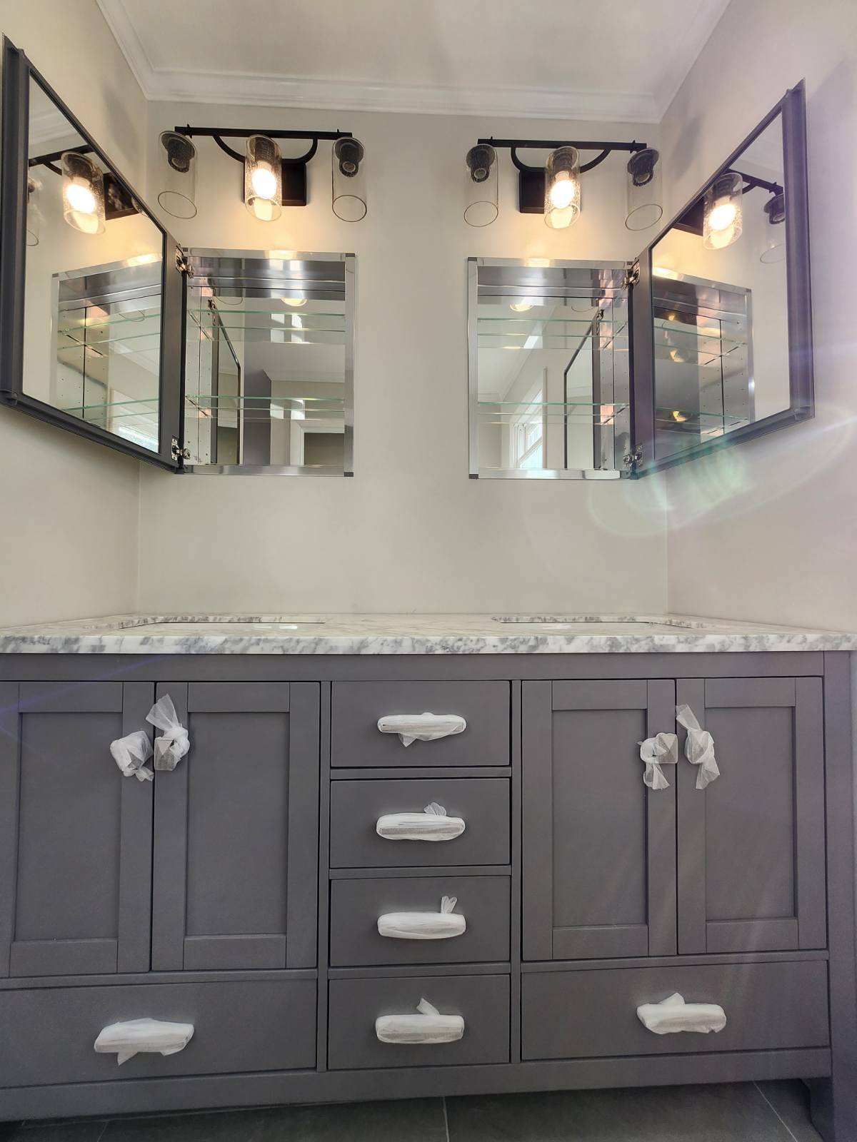 Gray vanity with marble countertop, two mirrored medicine cabinets, and sconce lighting.