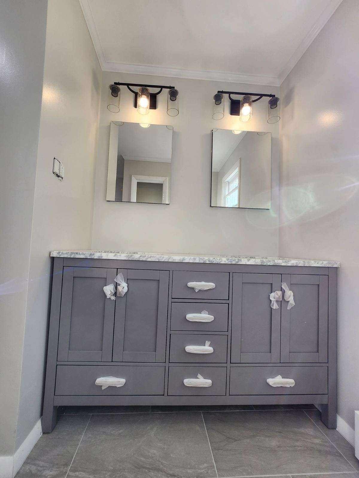 Gray bathroom vanity with marble countertop, two mirrors, and light fixtures.