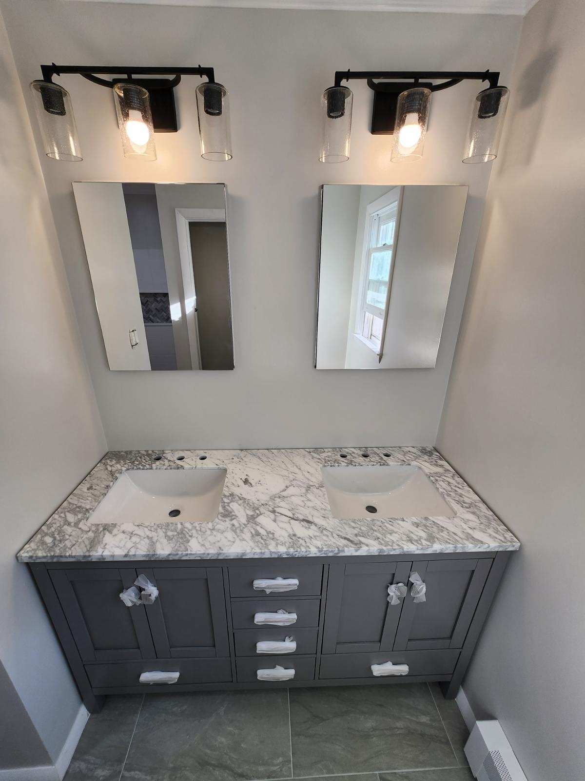 Bathroom with gray vanity, marble countertop, two sinks, mirrors, and black light fixtures.