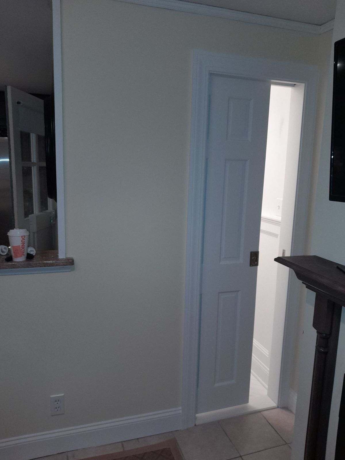 White door slightly ajar in a cream-colored room; doorway leads to a bright white space.