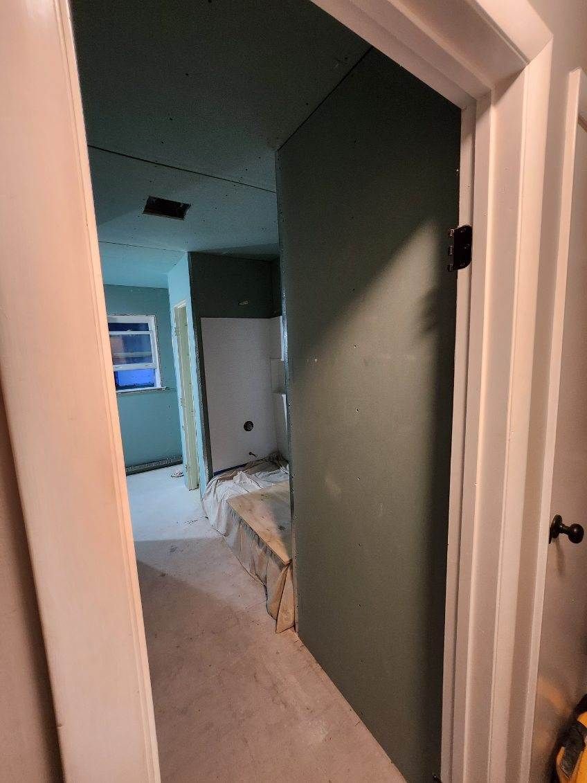 Bathroom under renovation, featuring green drywall, open doorway, and a partially finished shower.