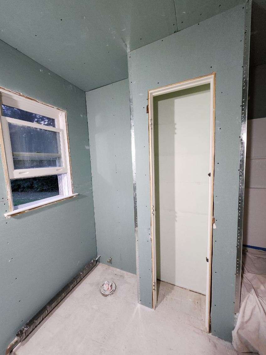 Interior of a room under construction, with green drywall, a window, and doorway.