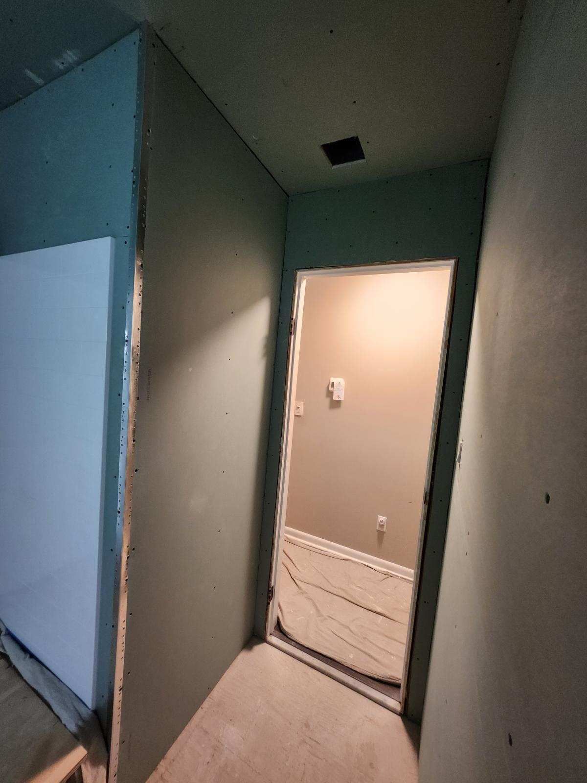 Interior hallway under construction; drywall, doorway, wires, and a ceiling opening.