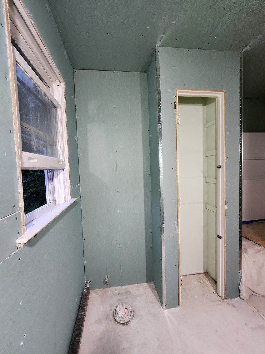 Interior room with pale green drywall, window on the left, doorway on the right, concrete floor.