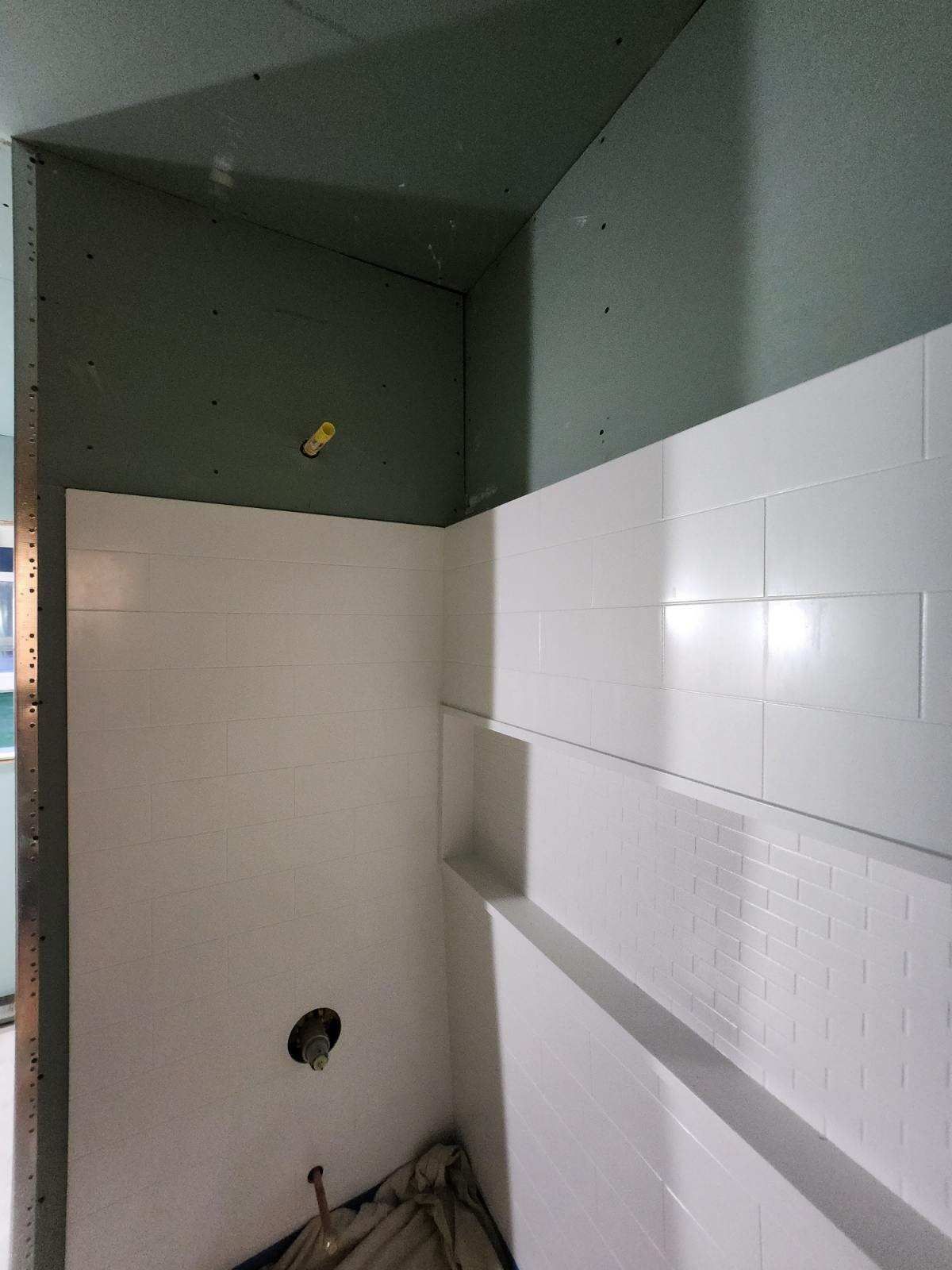 Shower stall under construction, featuring white walls, green drywall, and a plumbing fixture.