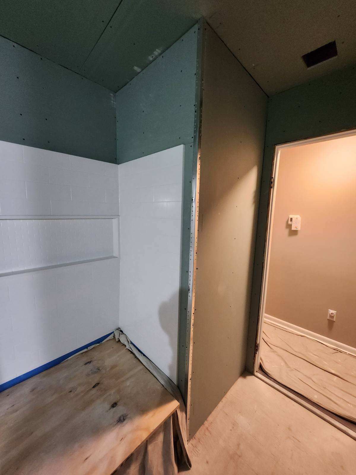 Corner shower stall with white walls and a light-colored wood base. The adjoining walls are green and tan.