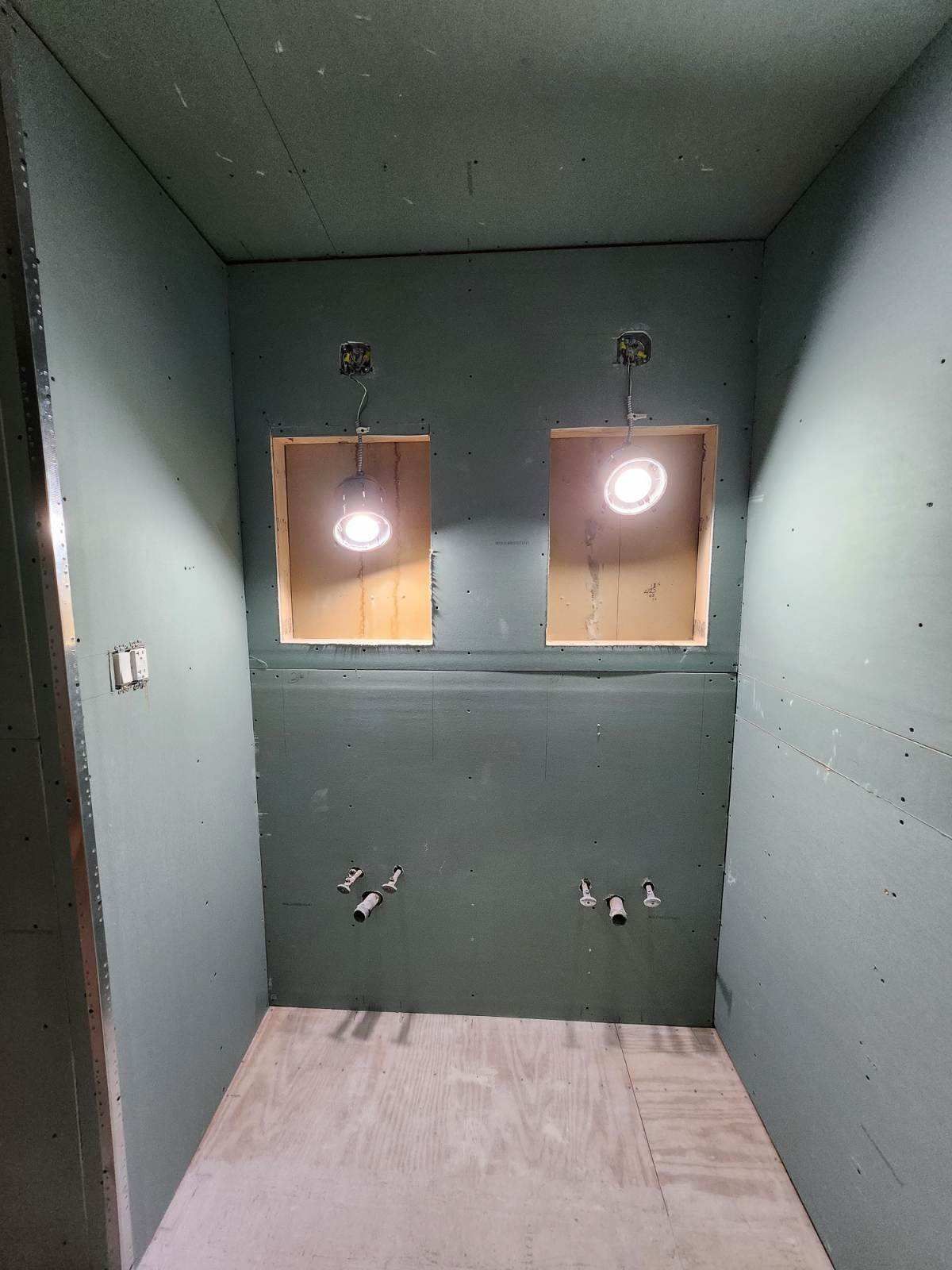 Empty bathroom under construction, teal walls, two recessed light boxes, plumbing fixtures, and bare concrete floor.