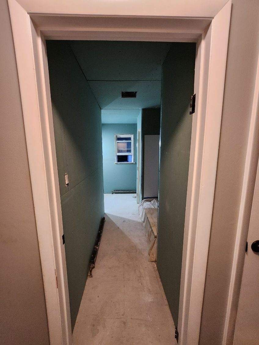 View down a narrow hallway with teal walls, white trim, and a window at the end.