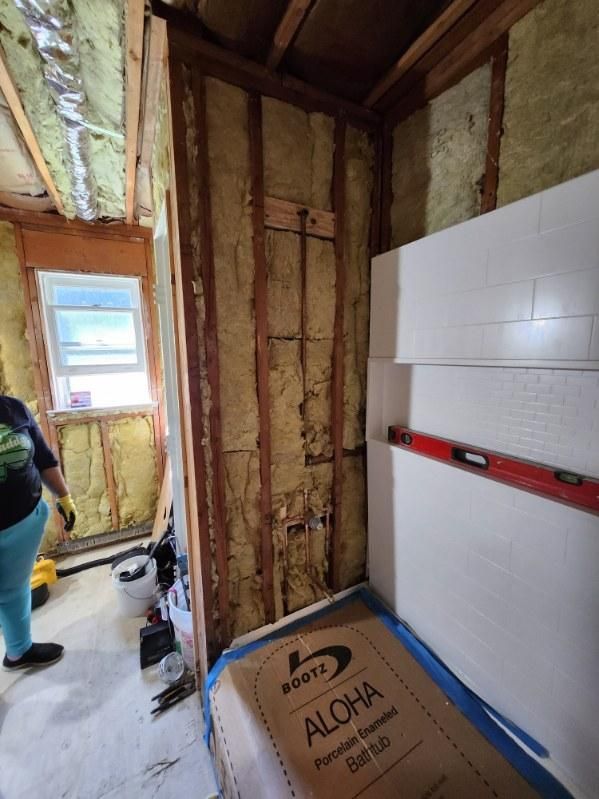 Interior framing with insulation visible. Foam boards stacked next to a stud wall. A person in the background.