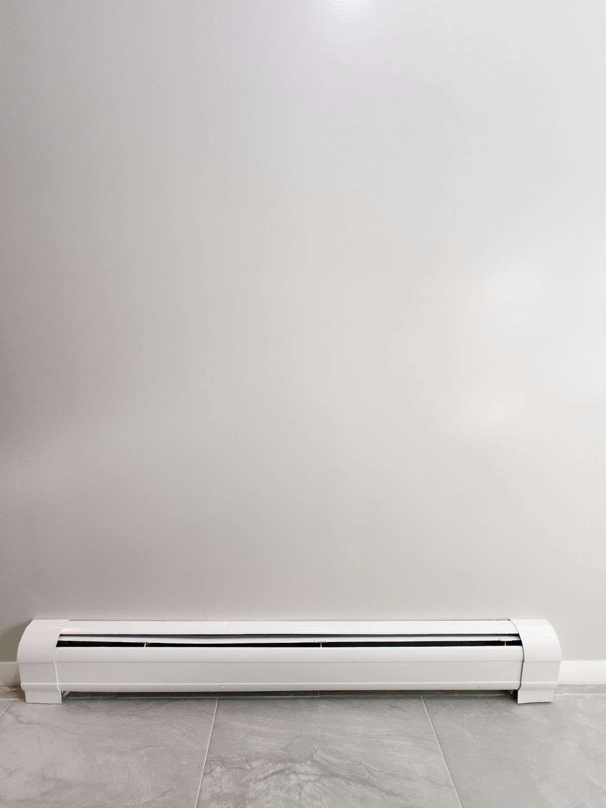 White baseboard heater against a light gray wall and floor.