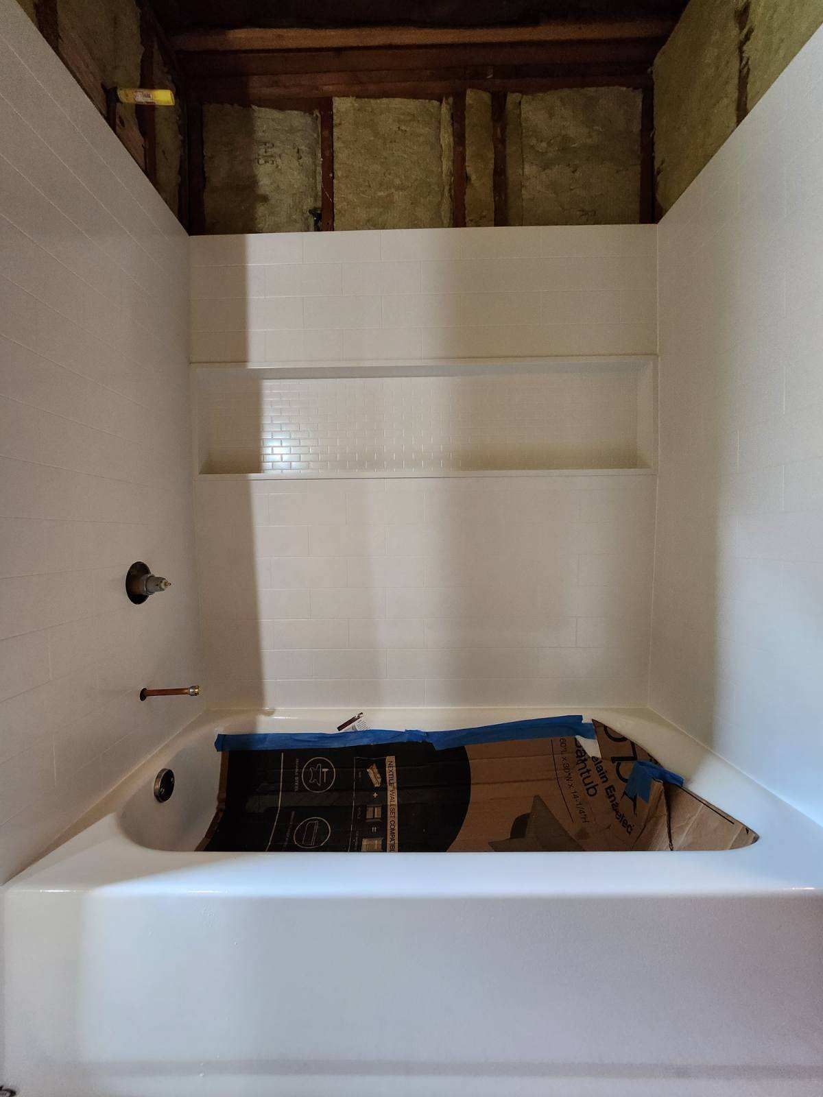 White bathroom with built-in shelves and a tub, under construction. Cardboard protects the tub.