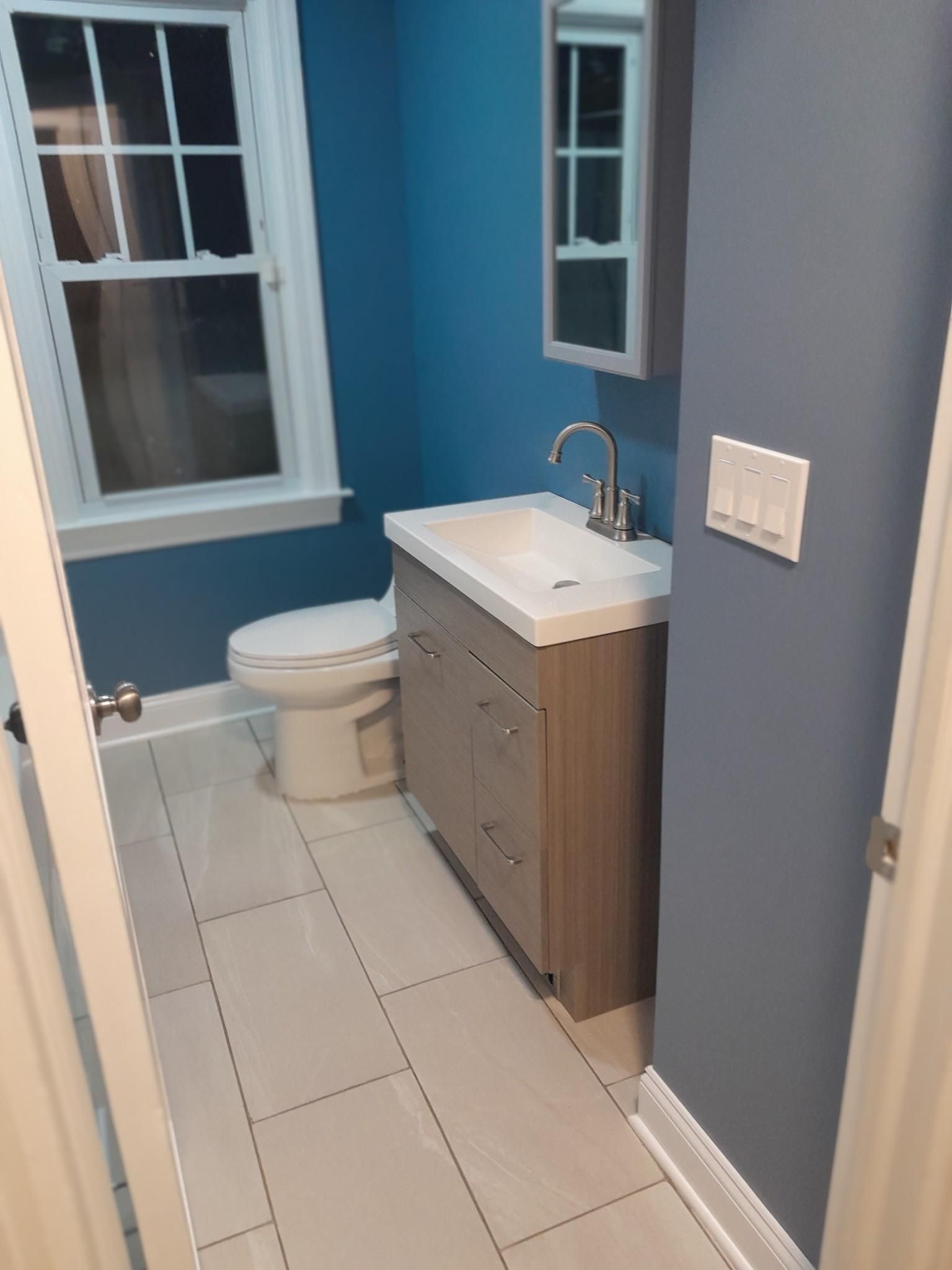 Bathroom with blue walls, a white sink and toilet, and light-colored tile floor.