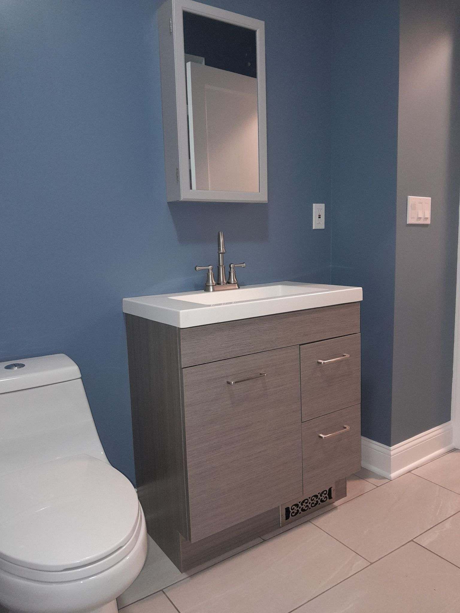 Bathroom with a gray vanity, toilet, and blue wall. A mirror hangs above the sink.