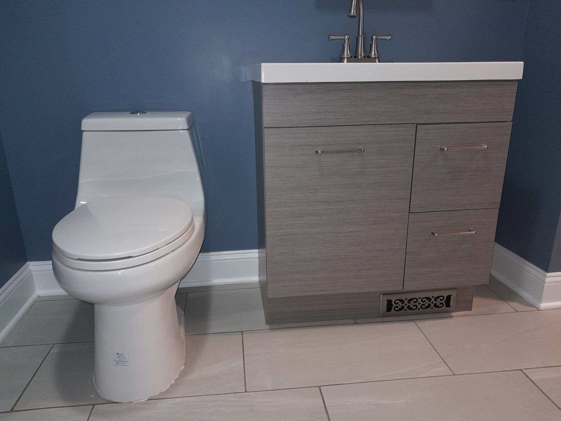 Toilet and bathroom vanity against a blue wall. Beige tile floor.