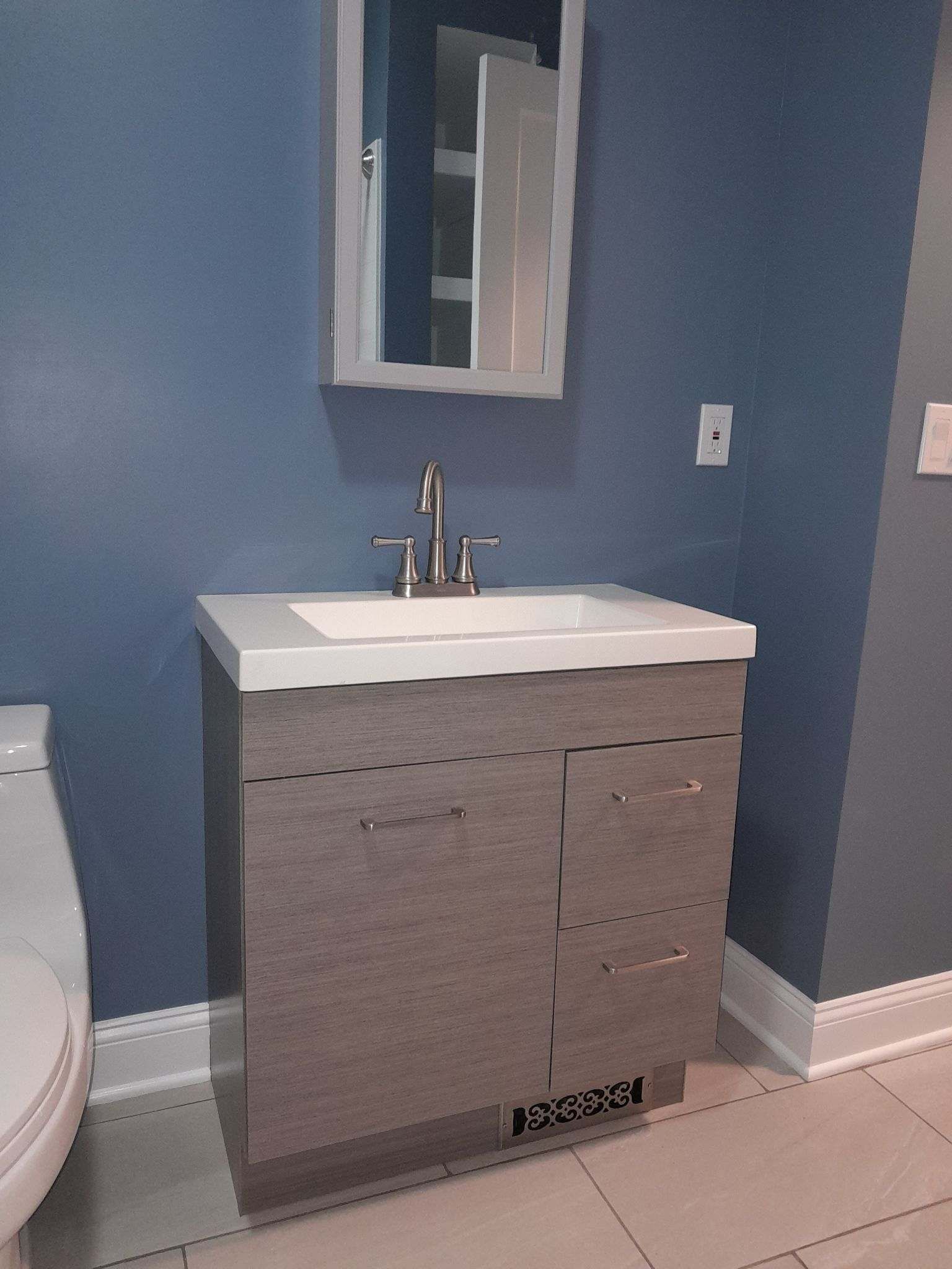 Bathroom with a gray vanity, white countertop, and blue walls. A mirror hangs above the sink.