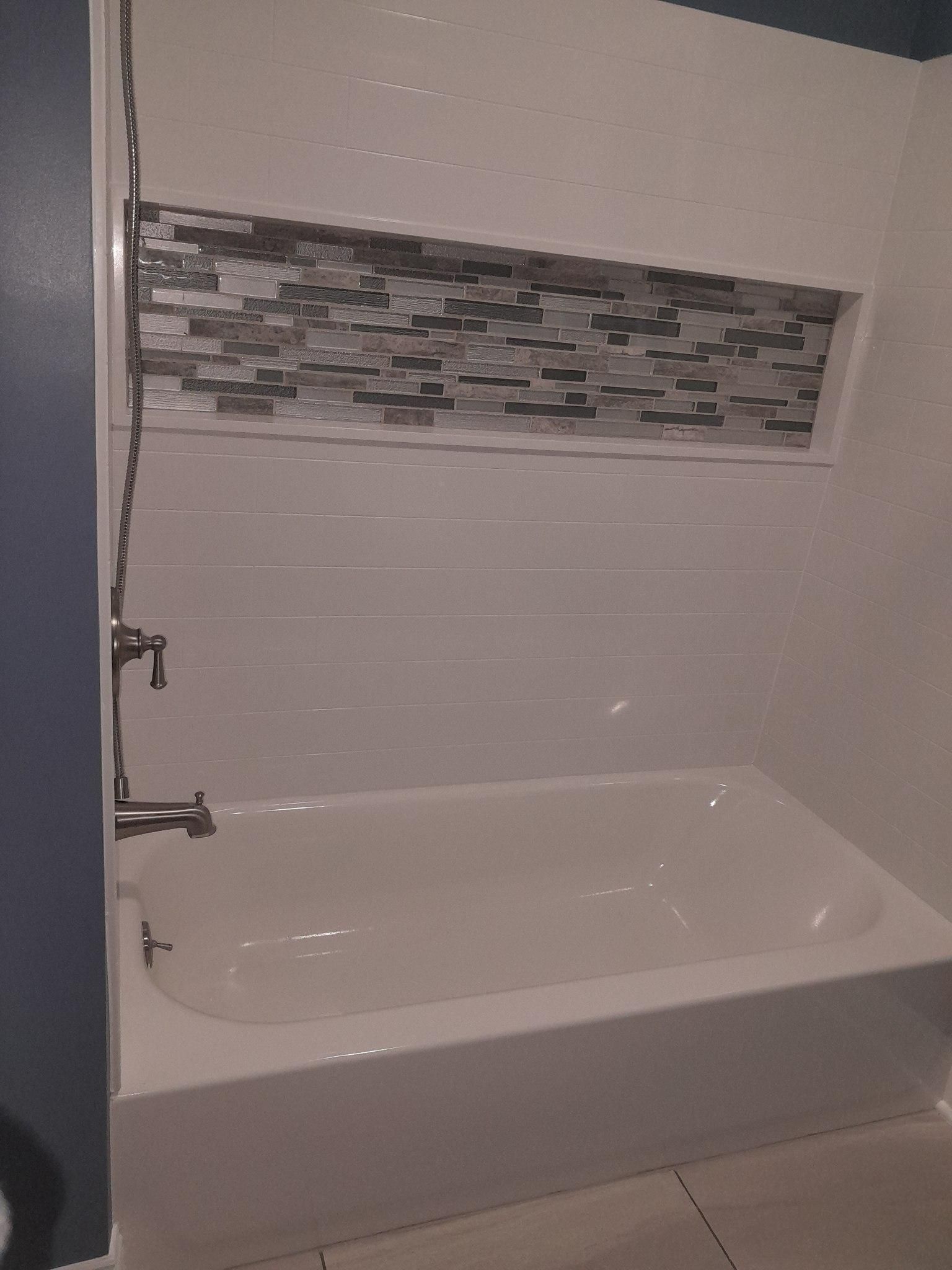 White bathroom with tub, showerhead, and decorative tiled alcove.