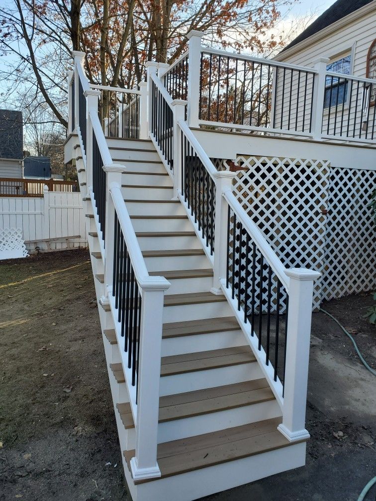 Wooden staircase with white posts, black railings, and a deck.