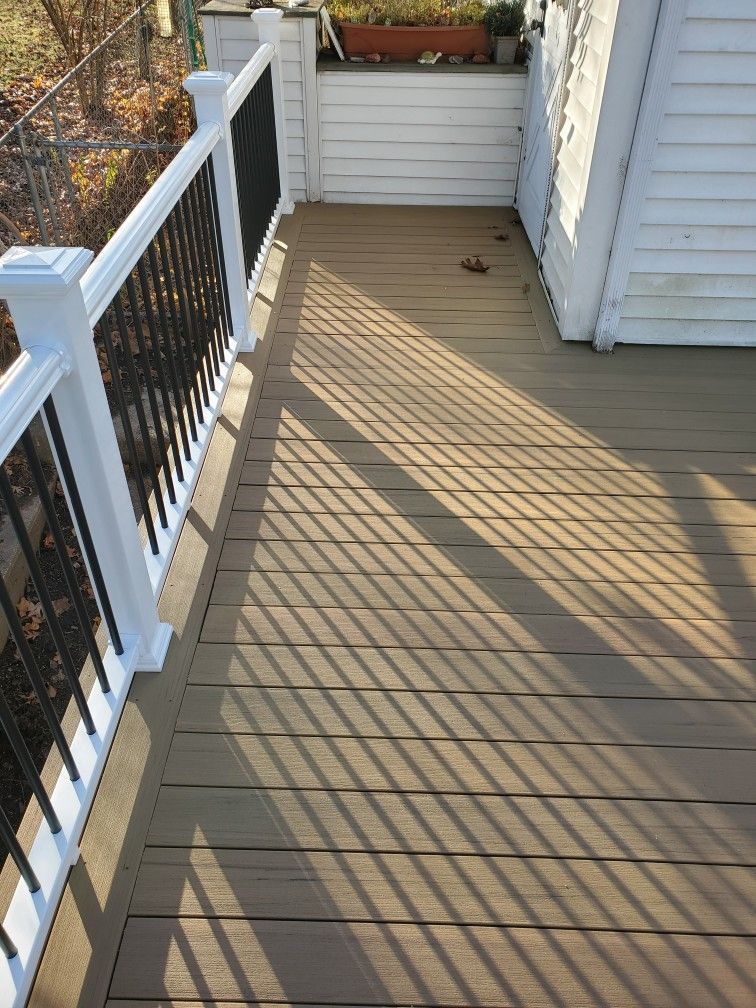 Deck with brown composite boards, white railing and black spindles, sunlight casting shadows.