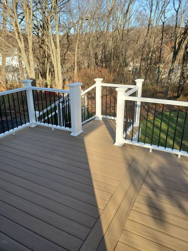 Brown deck with white railing posts, black spindles, and trees in the background.