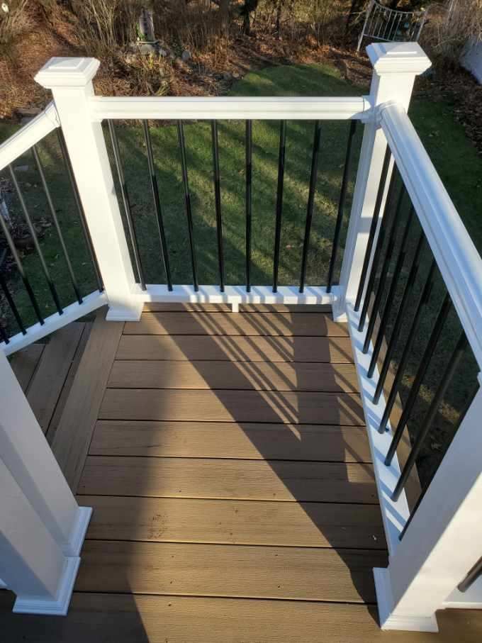 Deck with white railing and black spindles, viewed from above, casting long shadows.