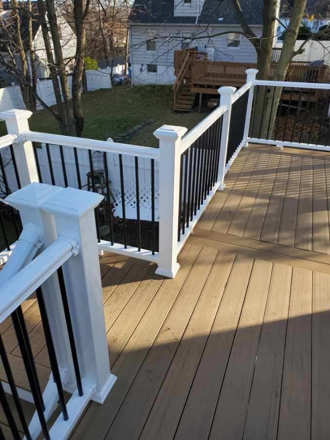A wooden deck with white railing posts and black balusters. Background includes a grassy yard and houses.