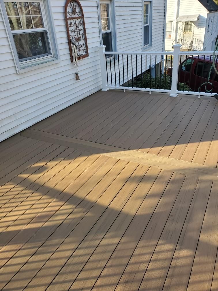 Brown composite deck with white railings and siding, cast shadows from the railing.