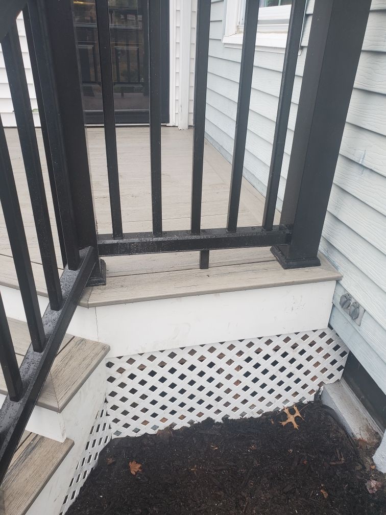 Black railing and posts on a porch with light gray steps and lattice trim.