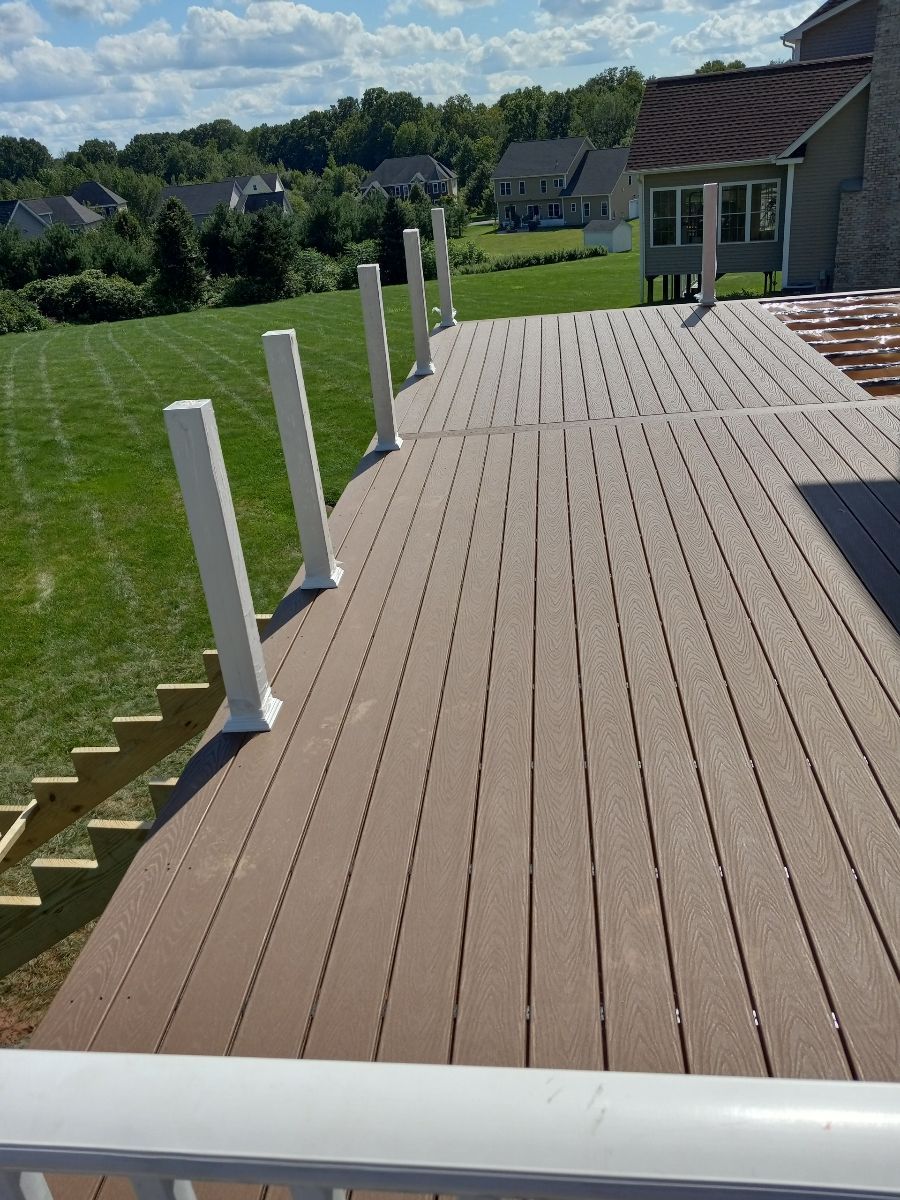 Composite deck with white posts, overlooking a green lawn and houses under a blue sky.