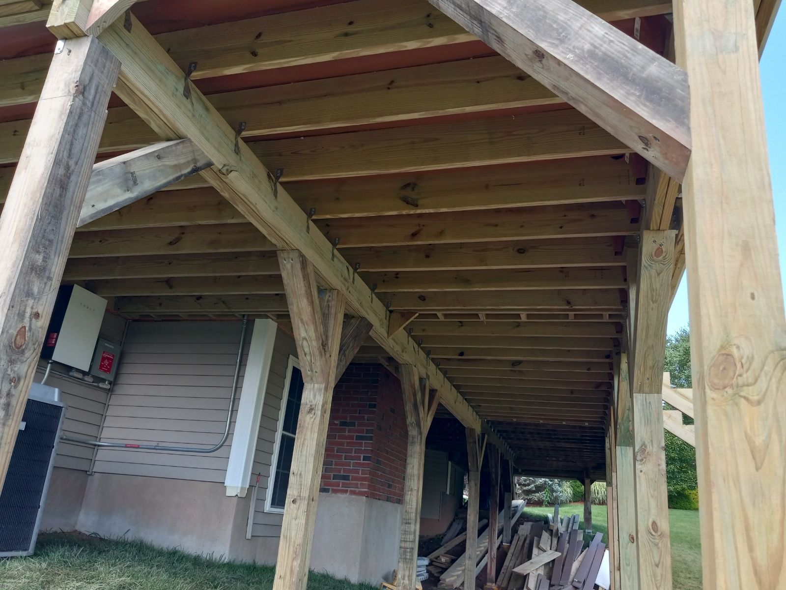 View of the underside of a wooden deck supported by posts, showing joists and construction in progress.