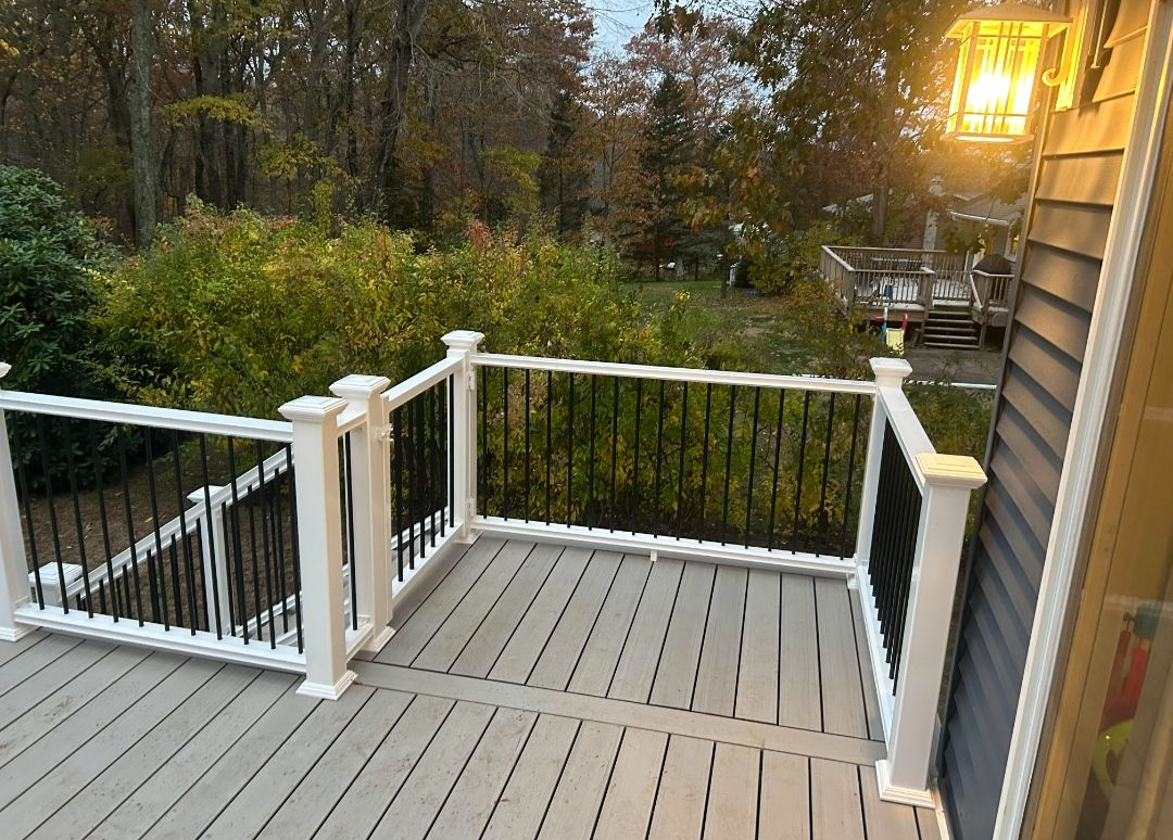 Deck with white posts, black railings, and gray floorboards overlooks a wooded area.