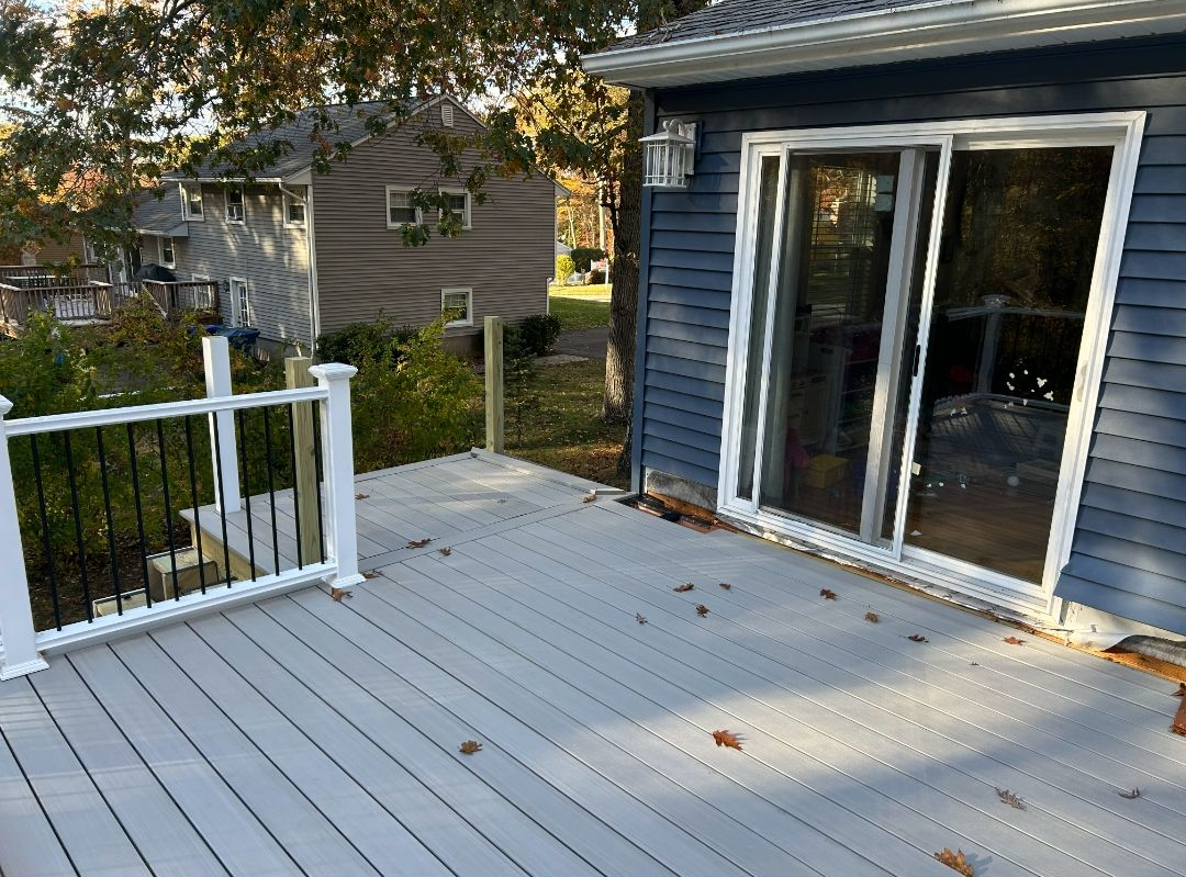 Gray deck with white railing, black spindles, and a blue house with sliding glass doors.