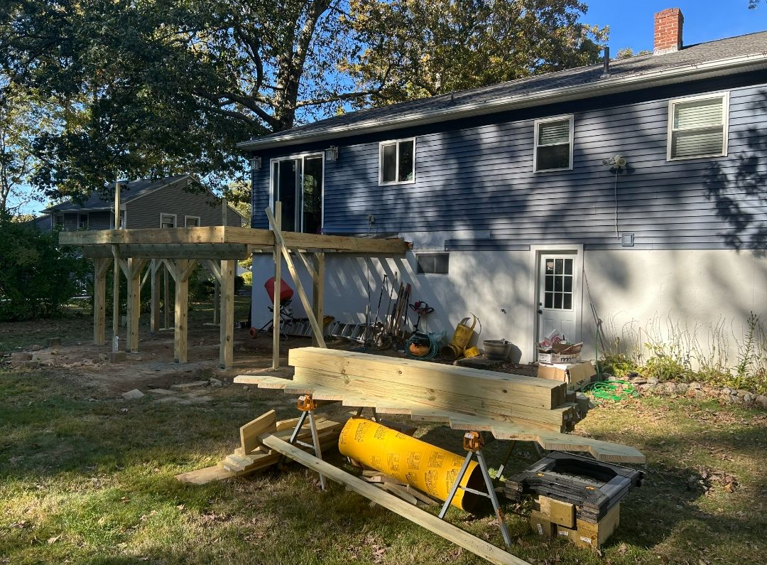 Backyard deck under construction; unfinished wooden frame attached to a blue house.