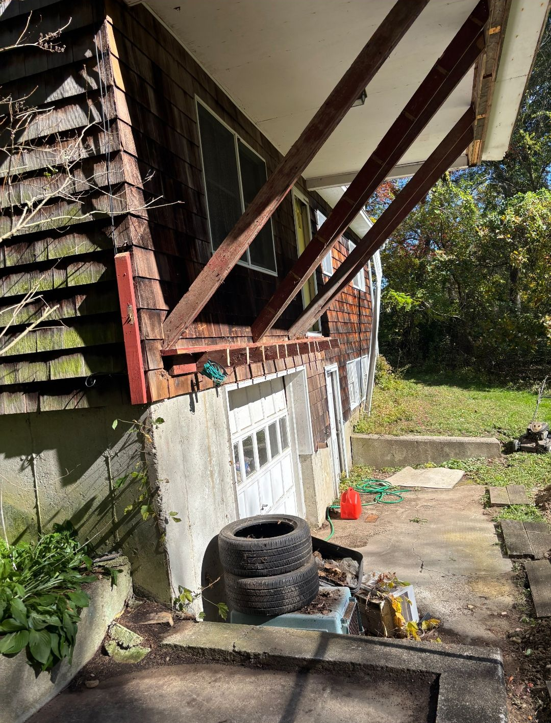 Exterior of a house with angled support beams, garage door, tires, and concrete foundation.