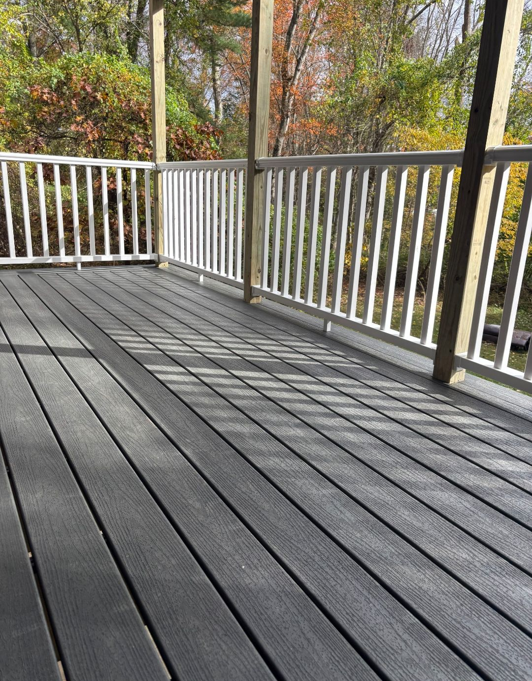 Gray composite deck with white railing, viewed from a slightly elevated perspective, surrounded by trees.